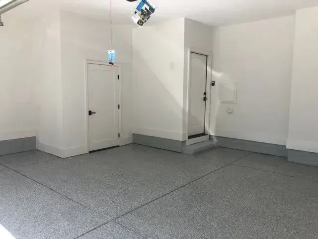 Empty garage interior with gray epoxy floor, white walls, and two doors.