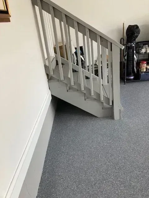 Gray painted staircase with railing, against a white wall and blue carpet.