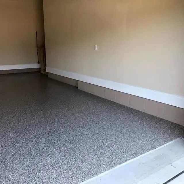 Gray speckled epoxy garage floor with tan walls and white baseboard.
