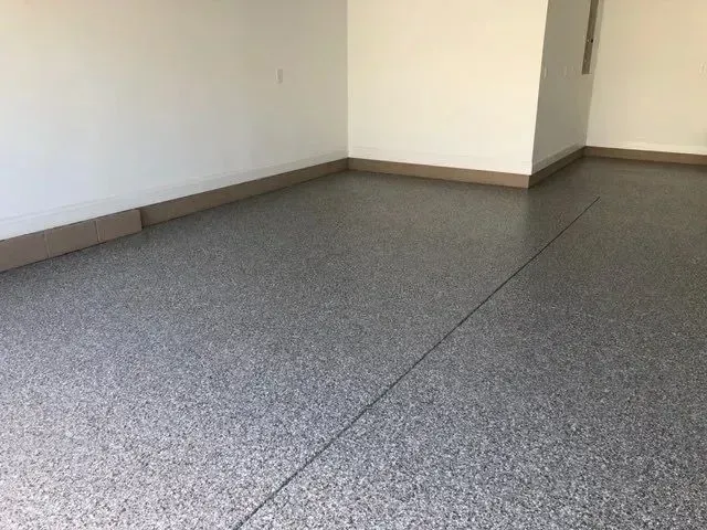Garage interior with gray speckled epoxy floor and tan baseboards. White walls.