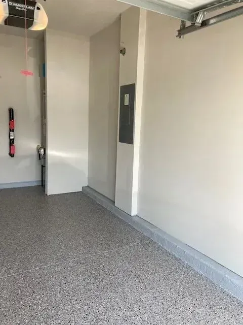 Garage interior with speckled gray floor and light-colored walls. A utility panel is visible on a wall.