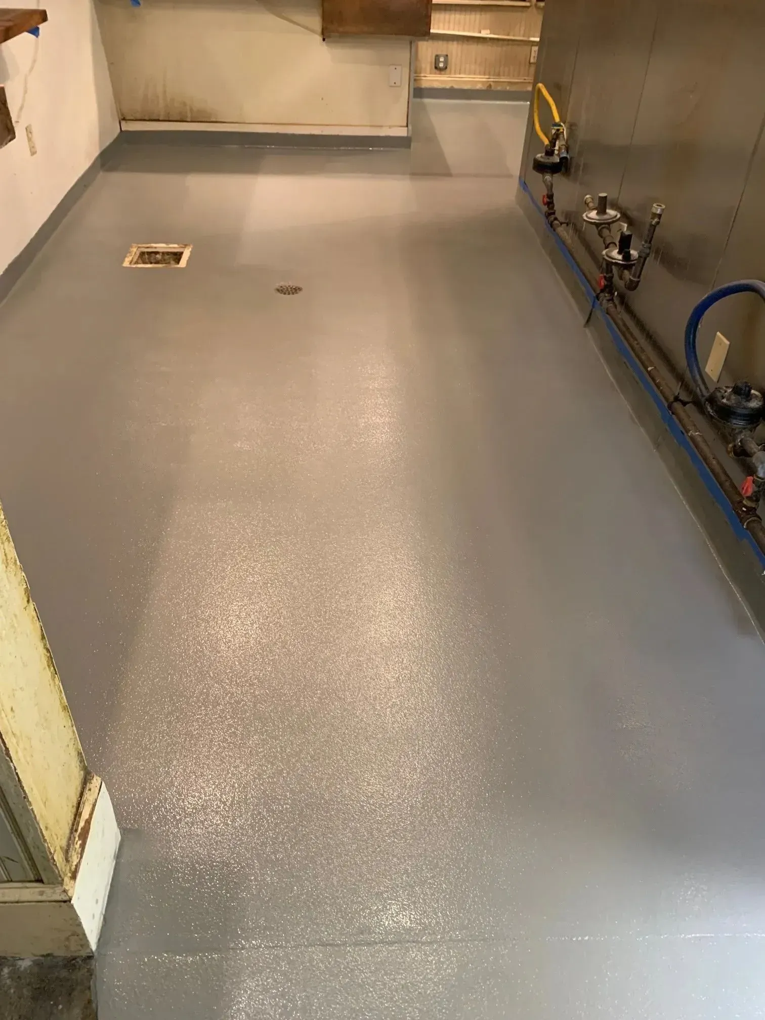 Grey painted concrete basement floor with utility pipes along the right wall.