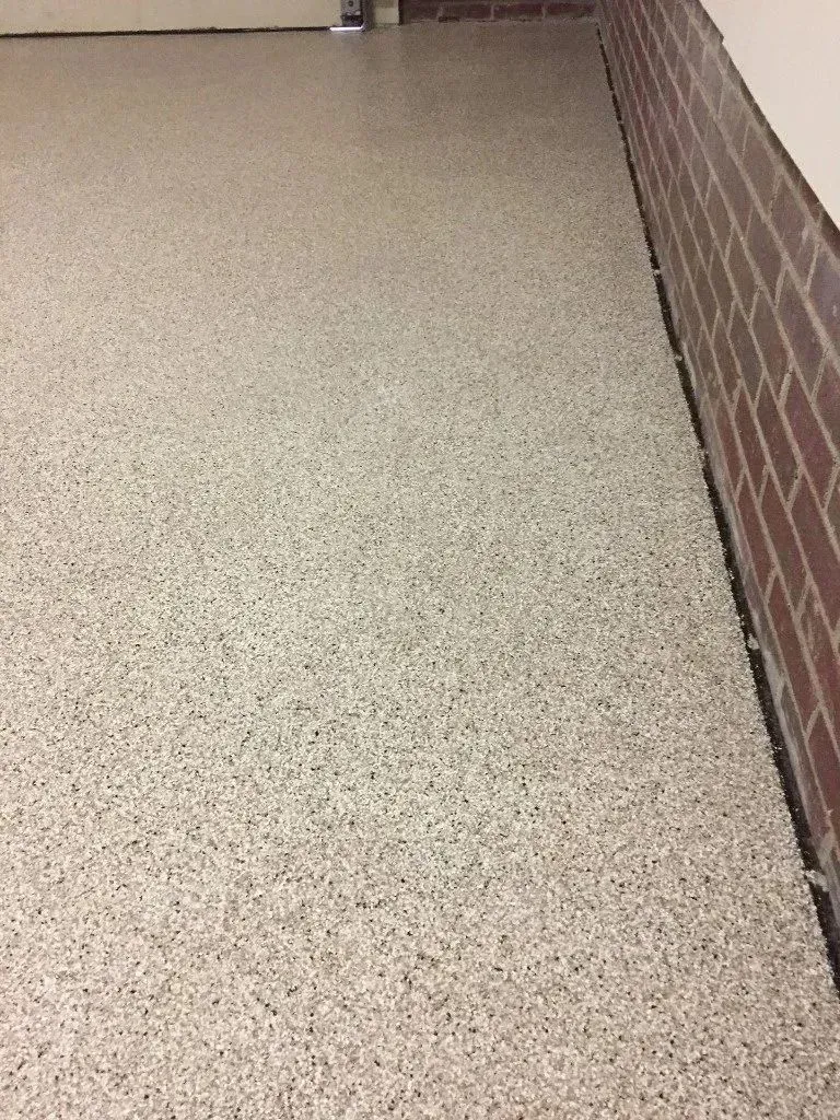 Epoxy-coated garage floor with speckled gray, white, and black chips. Red brick wall on the right.