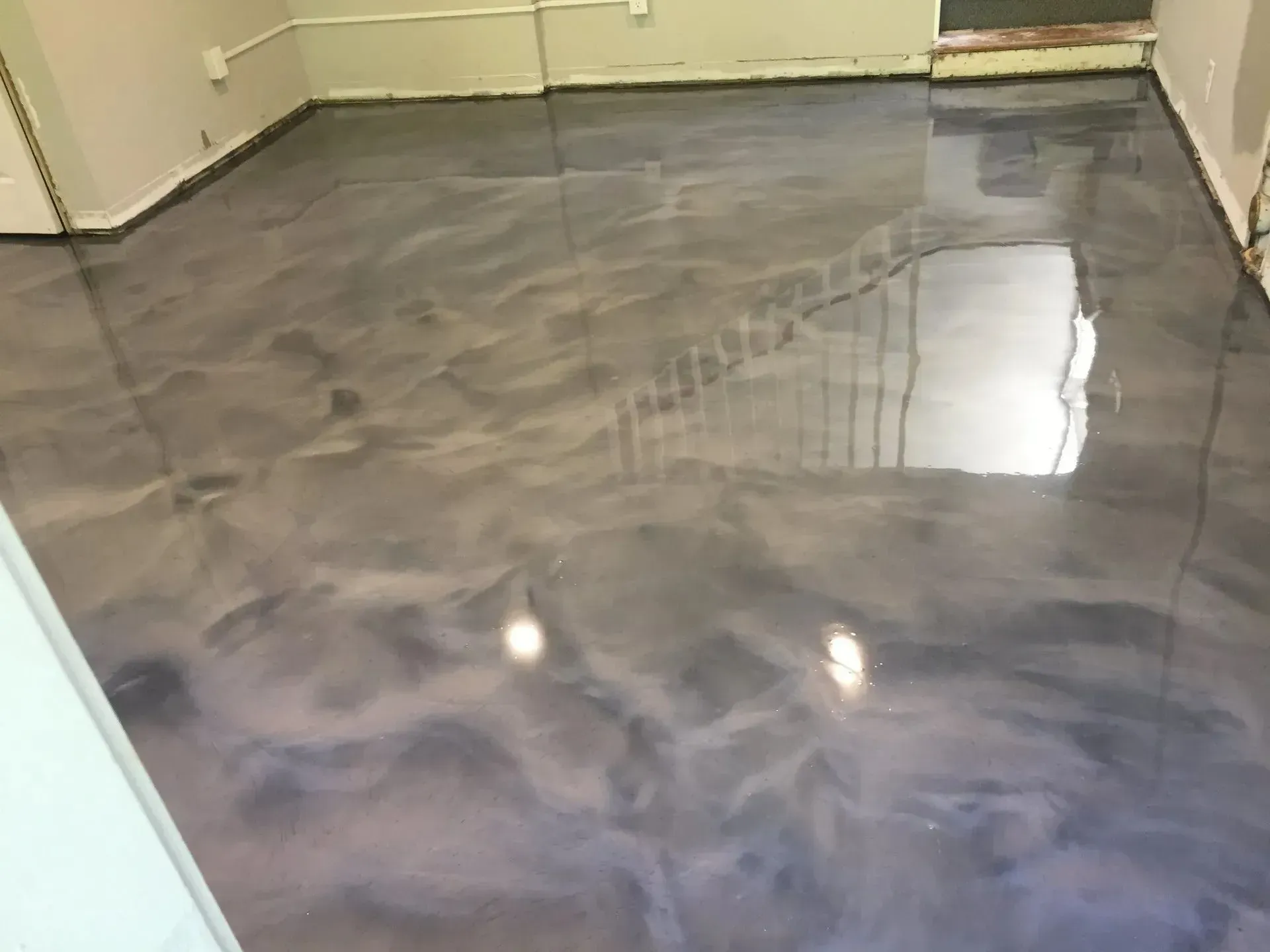 Metallic gray epoxy flooring reflects light in a room, with a staircase visible in the reflection.