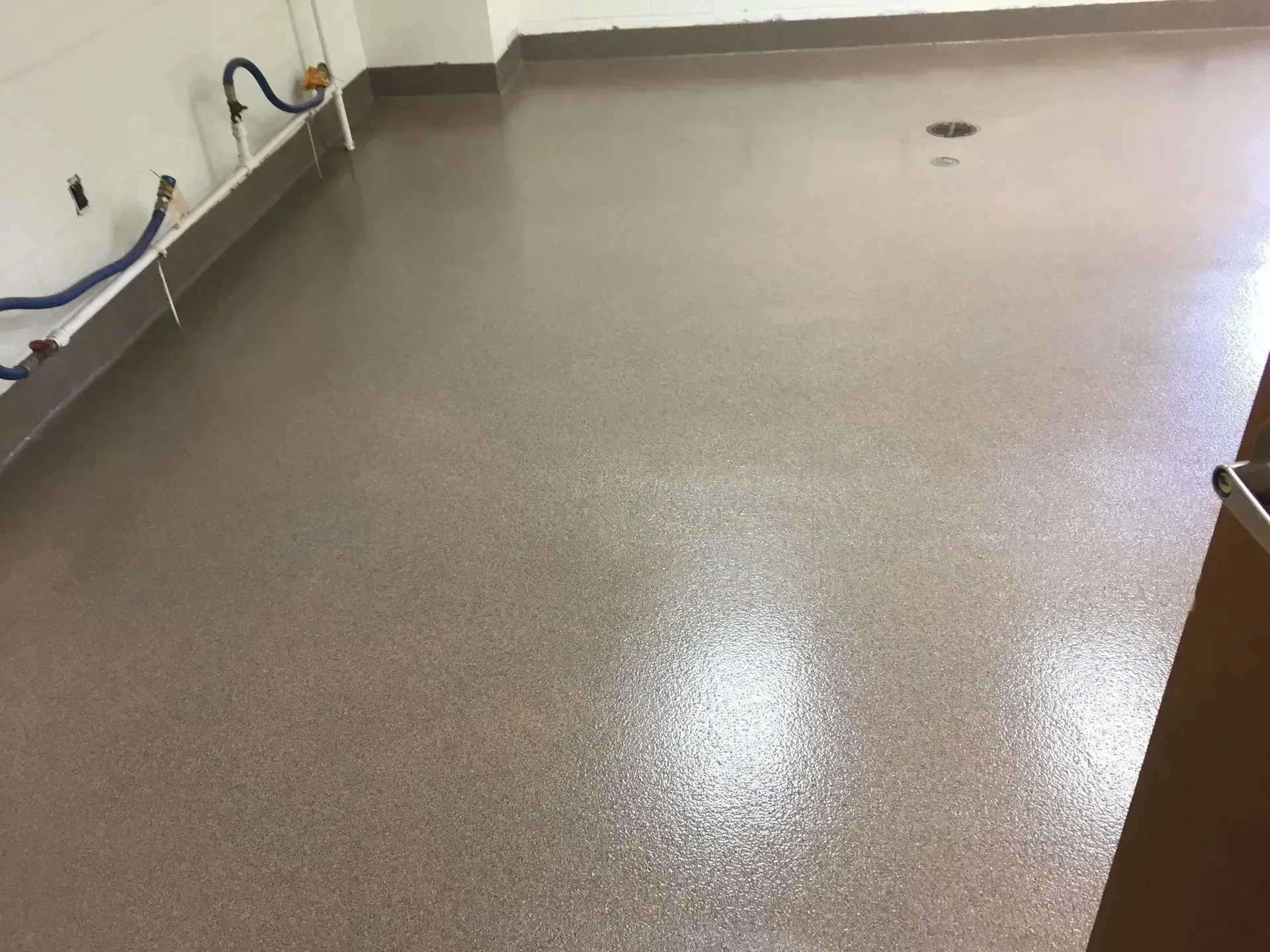 A floor covered in a speckled, shiny, brown epoxy resin with a dark brown baseboard.