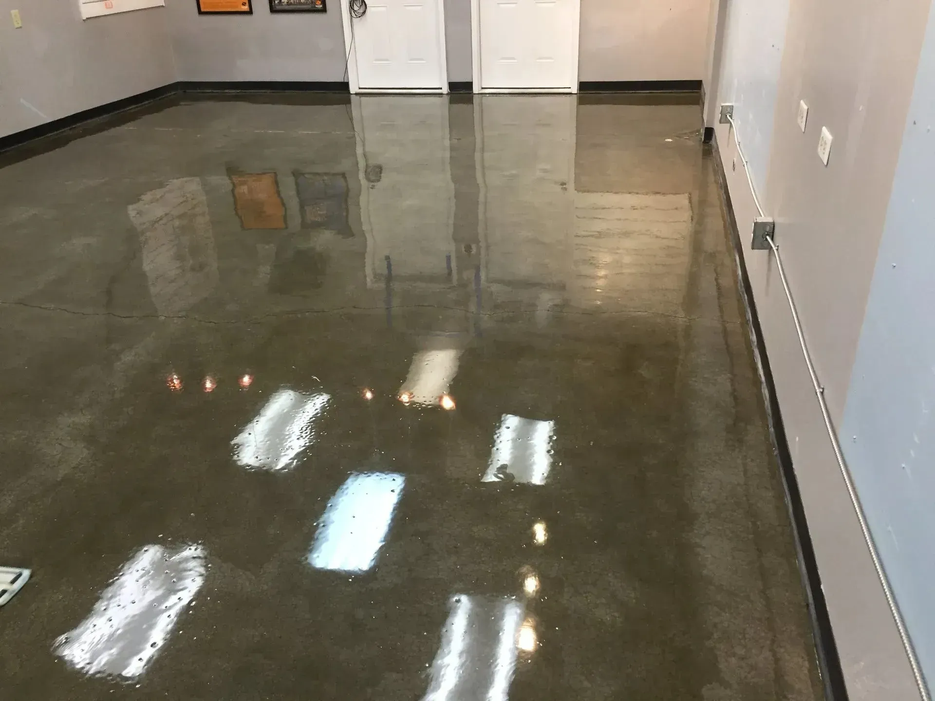 Shiny, gray concrete floor in a room with white walls, two white doors, and some scattered white markings.