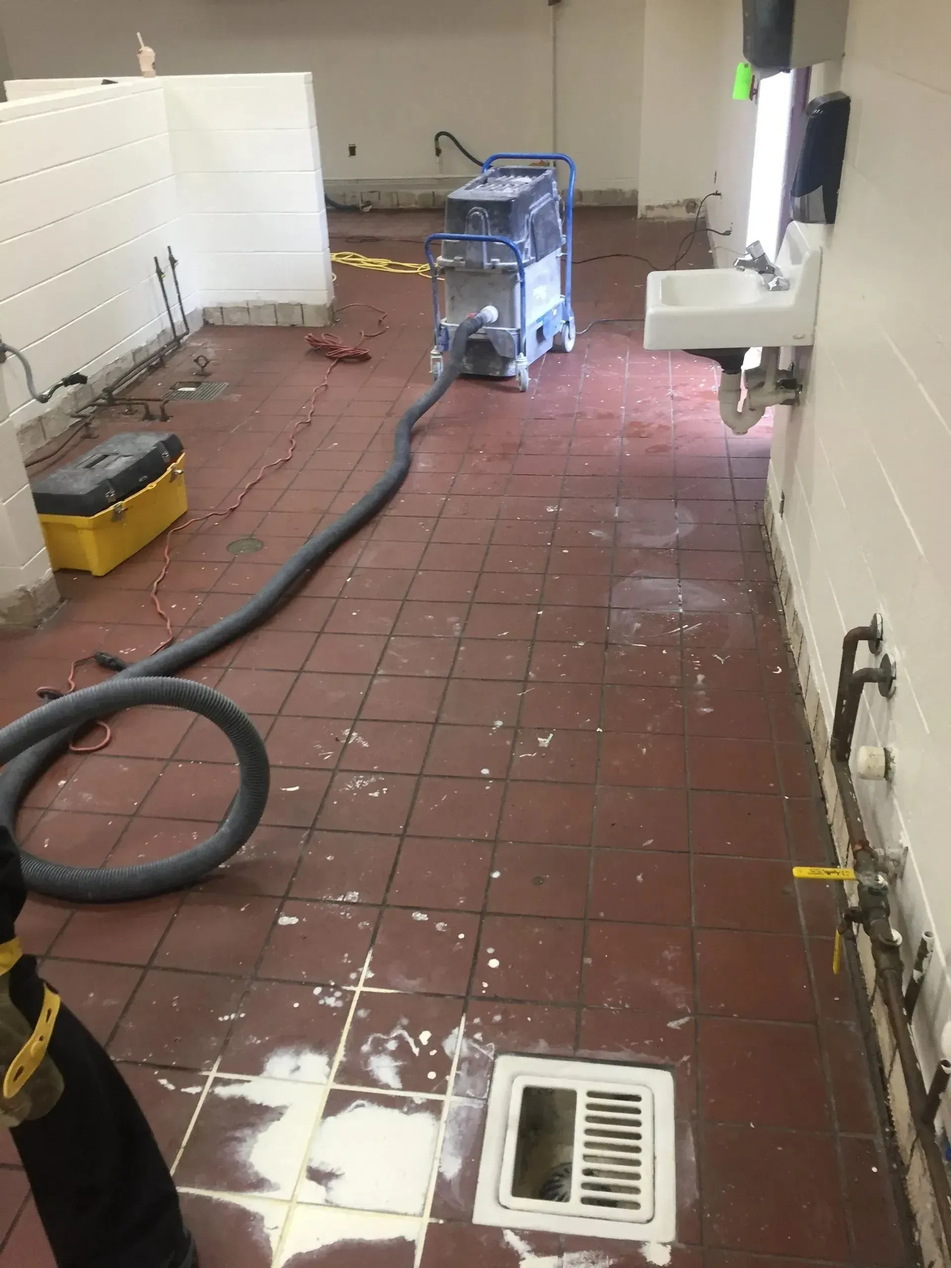 A room with a water extraction machine, wet floor, and white tiled walls.