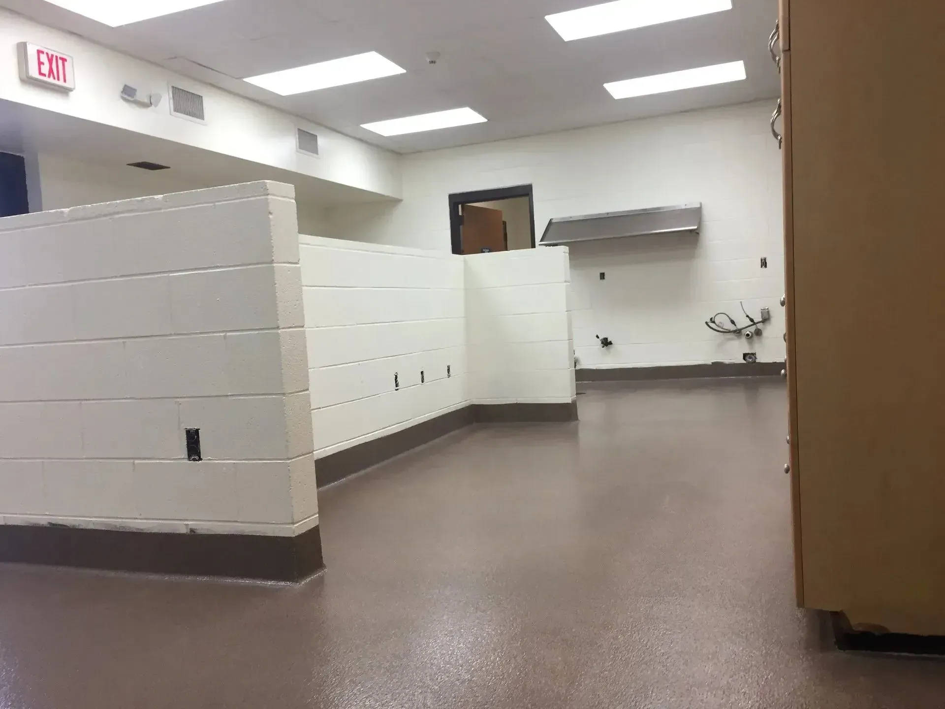 Empty commercial kitchen with white dividers, brown floor, and stainless steel hood.