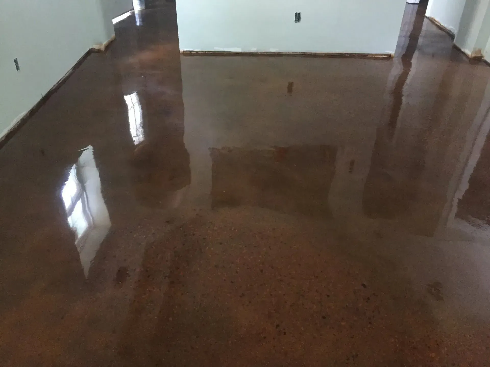 Shiny, metallic-brown epoxy floor reflecting the windows and walls in an empty room.