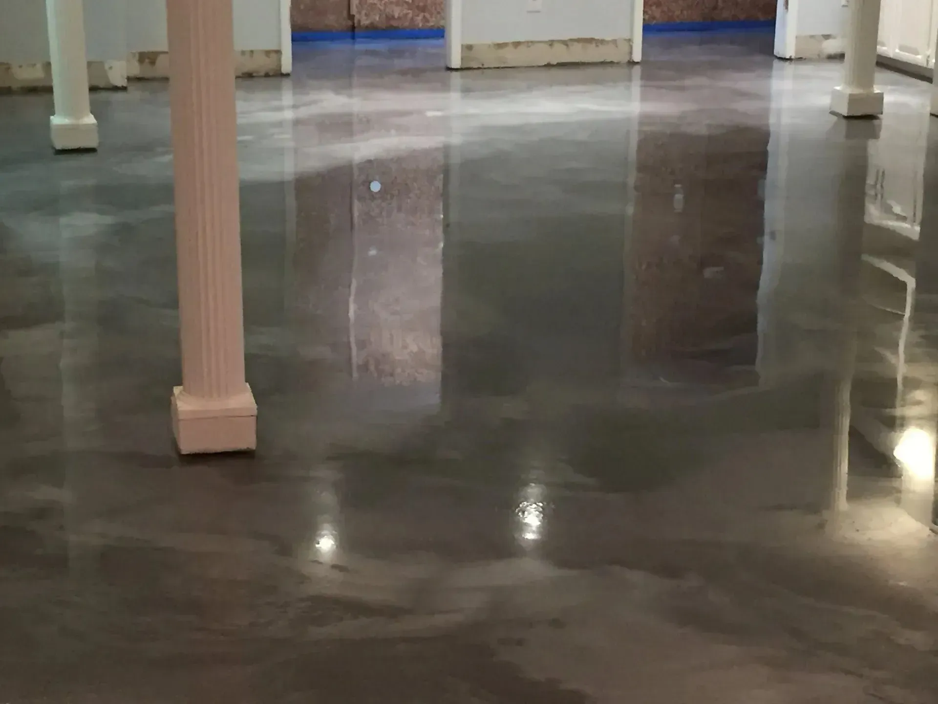 Polished concrete floor with reflective sheen in a room with columns; neutral color palette.