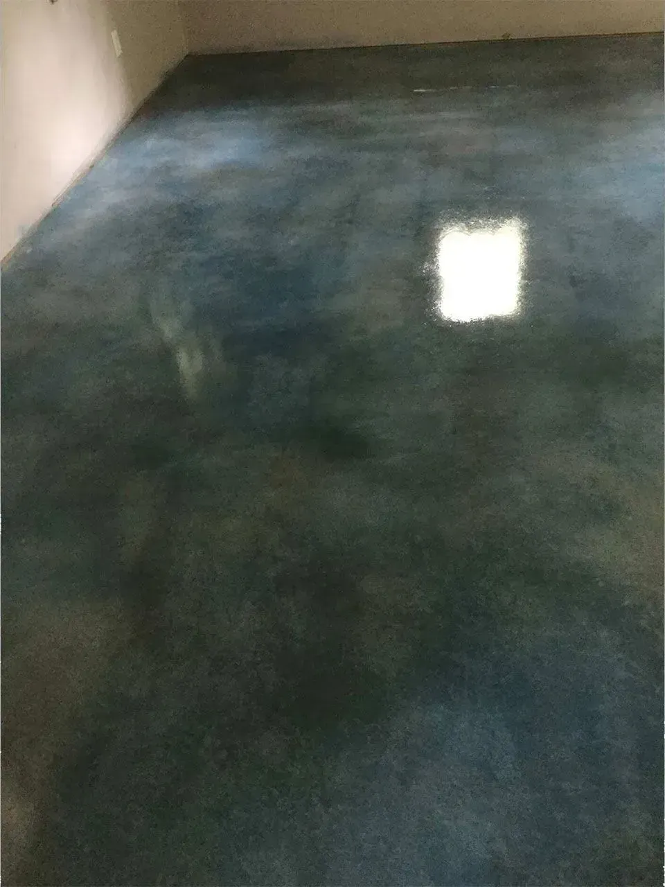 Blue-toned concrete floor with a glossy finish, reflecting a square of light.