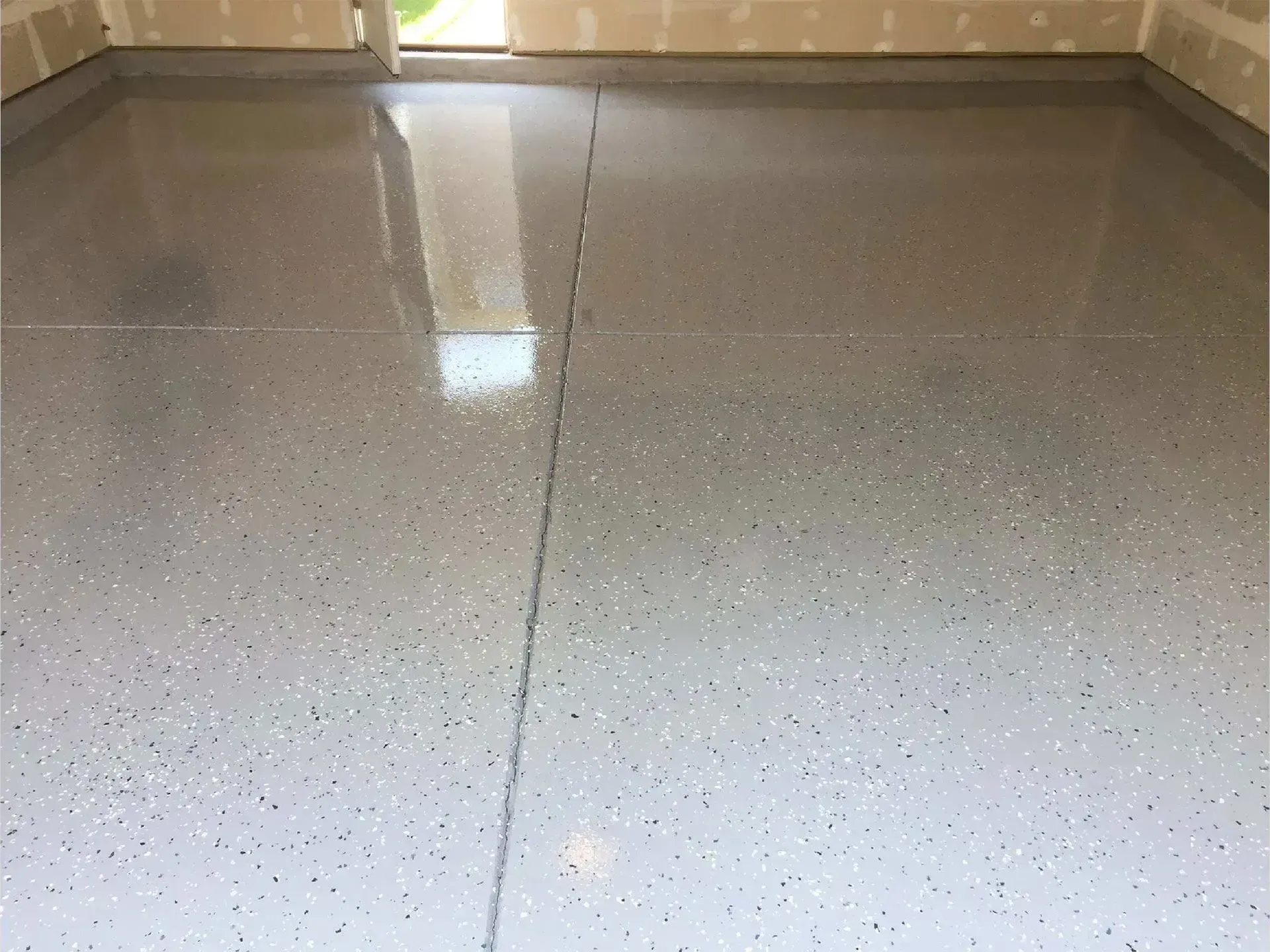 Epoxy-coated garage floor, speckled gray, with a shiny, reflective surface.