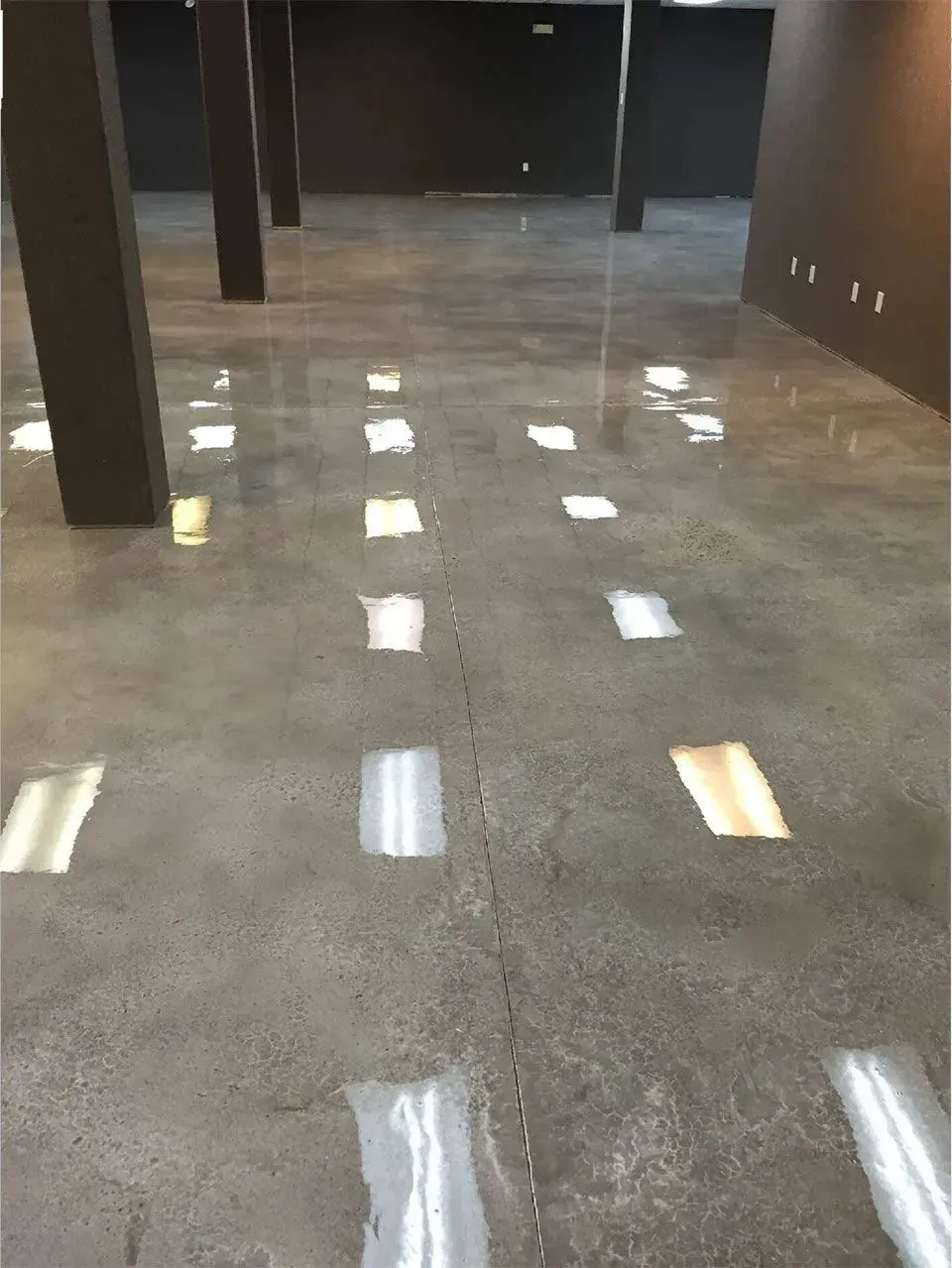 Polished concrete floor with column supports, reflecting light. Dark walls.