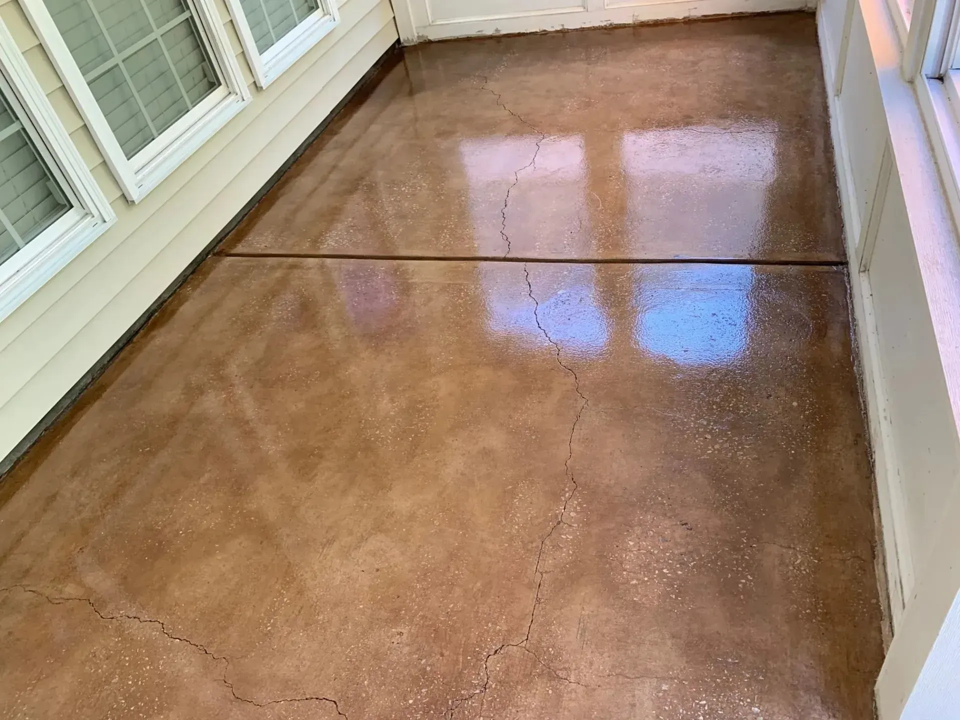 Brown stained concrete patio with cracks, reflecting light near a house.