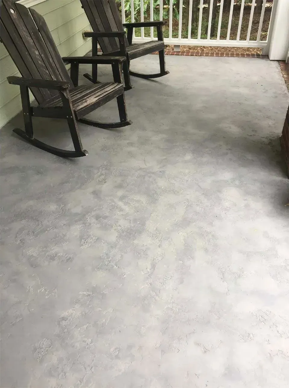 Two rocking chairs sit on a gray concrete porch.