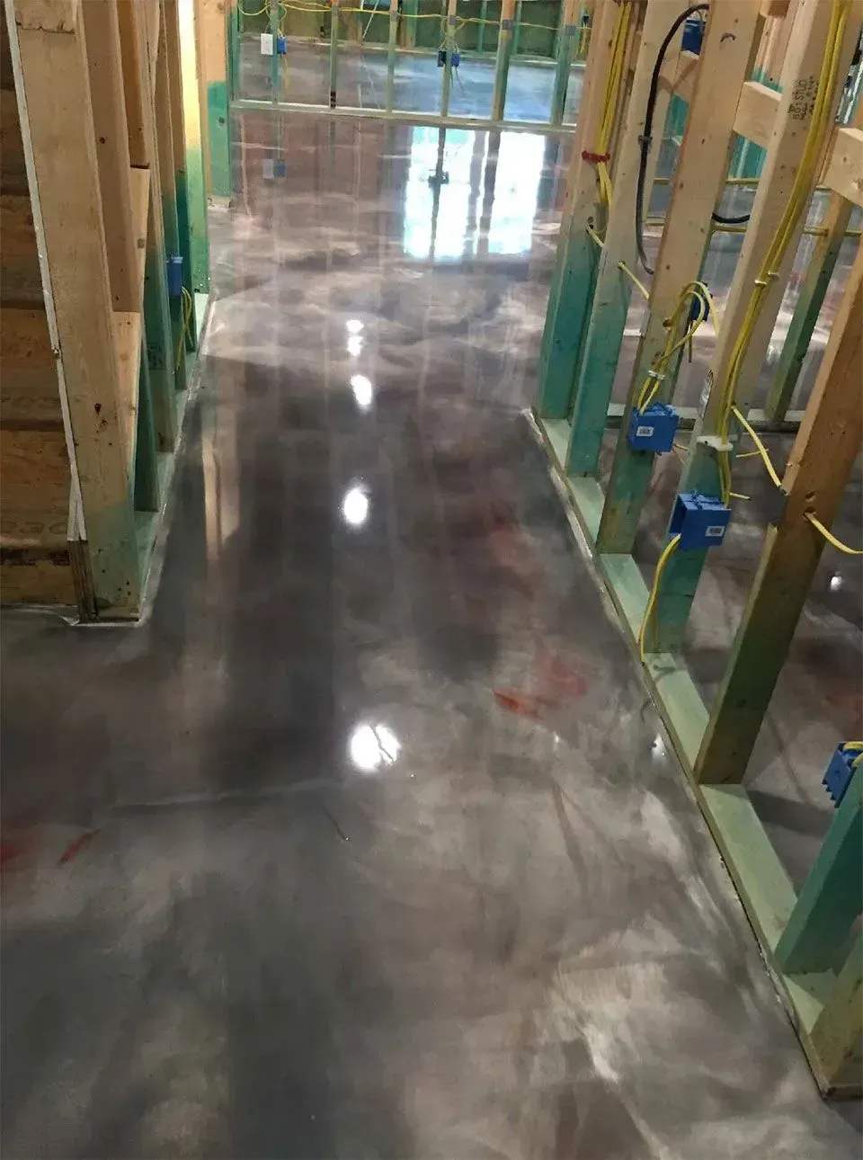Metallic epoxy floor under construction, gray and silver tones, surrounded by wood framing.