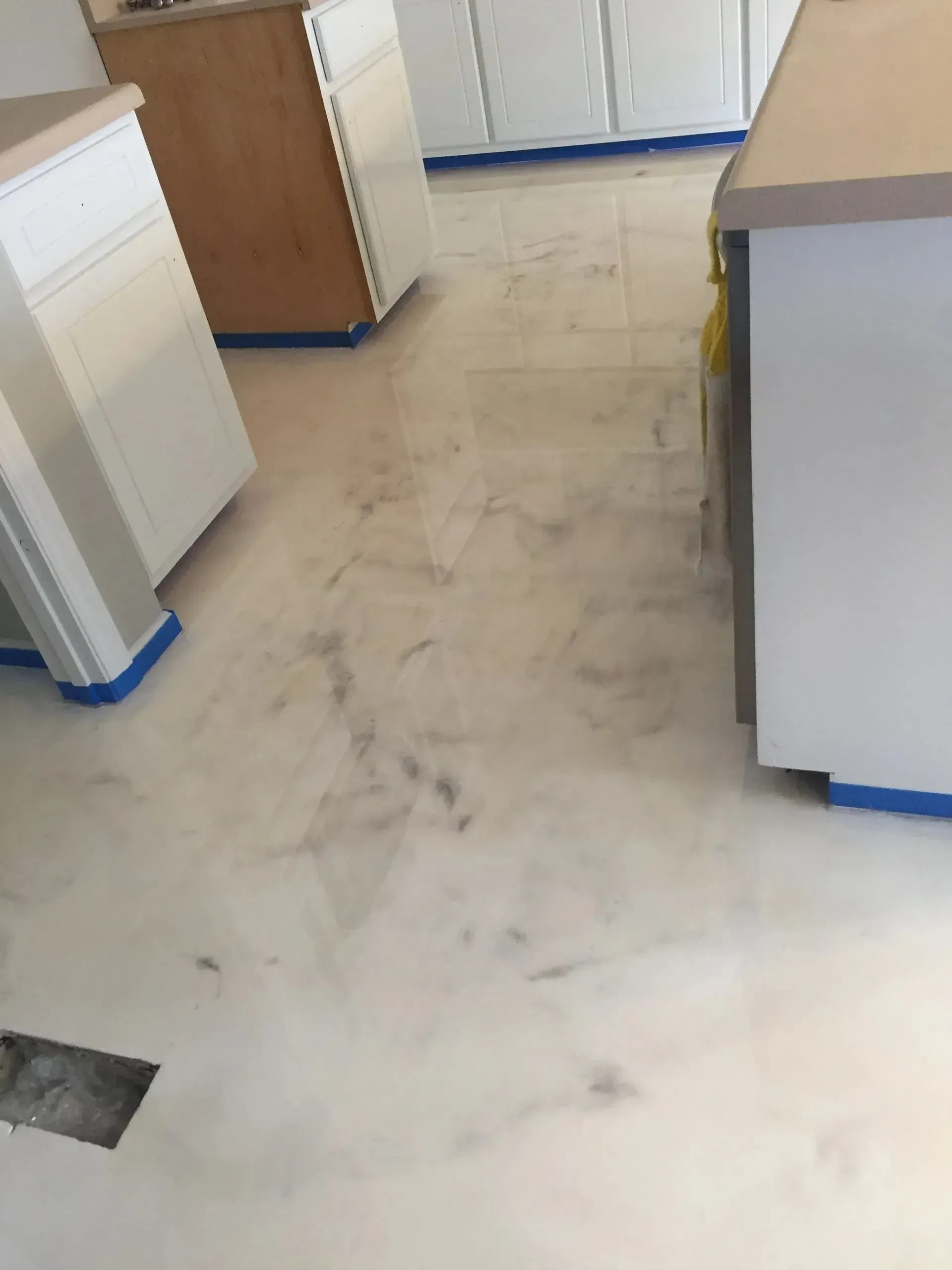 Kitchen undergoing renovation with light-colored flooring and white cabinets, blue painter's tape visible.