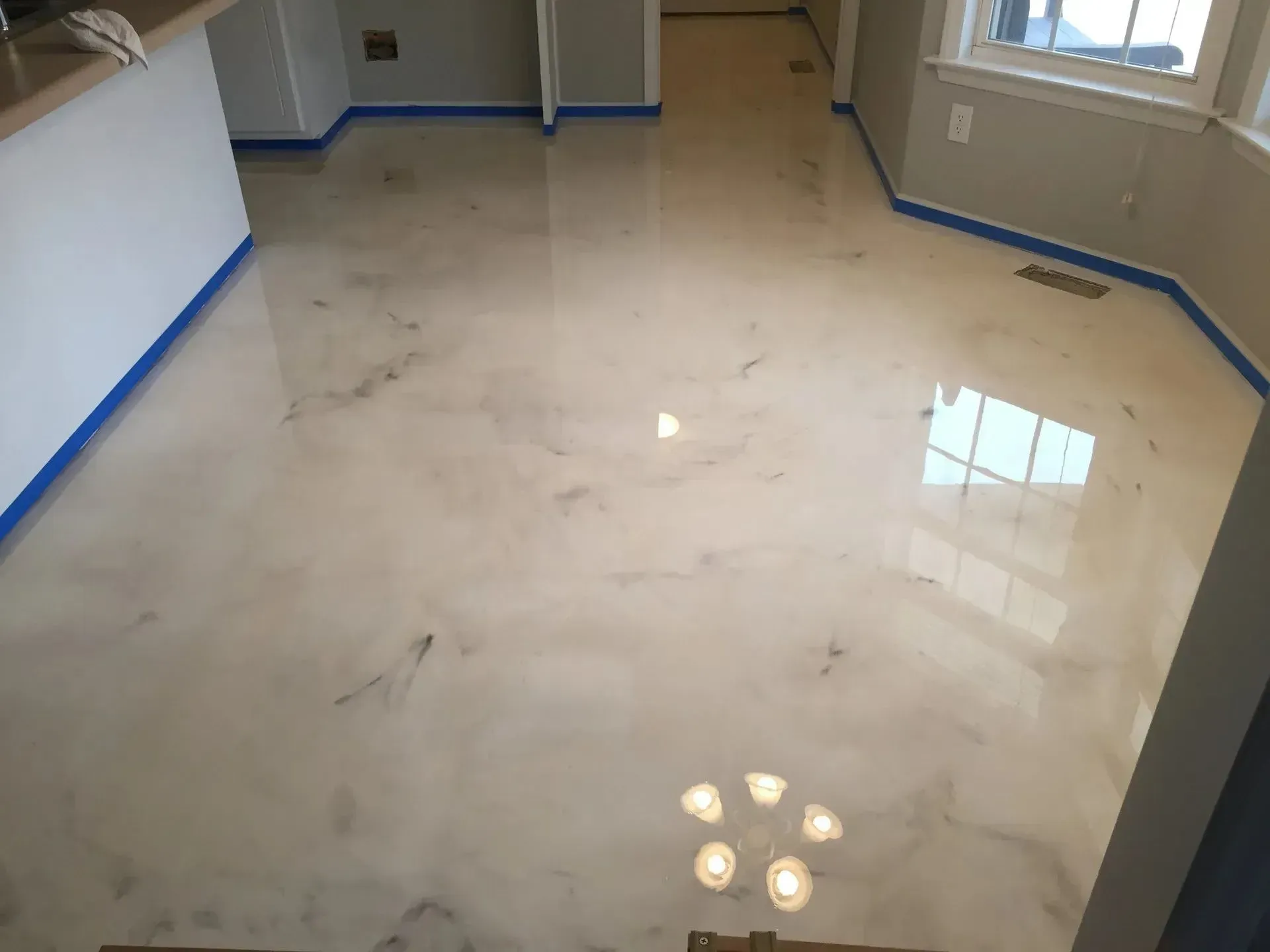Shiny, cream-colored epoxy floor with gray marbling, blue tape around the edges, and window reflection.