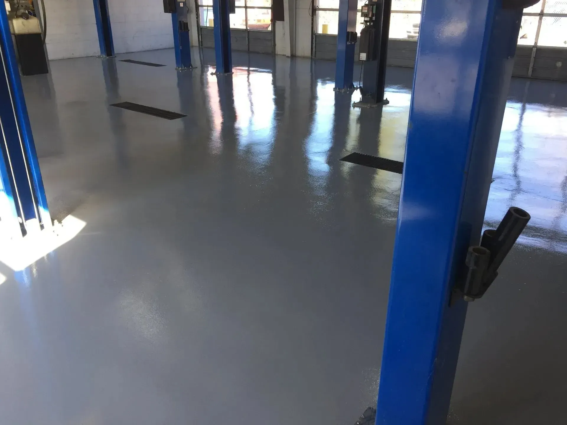 Gray epoxy-coated floor in a garage with blue support columns reflecting light.