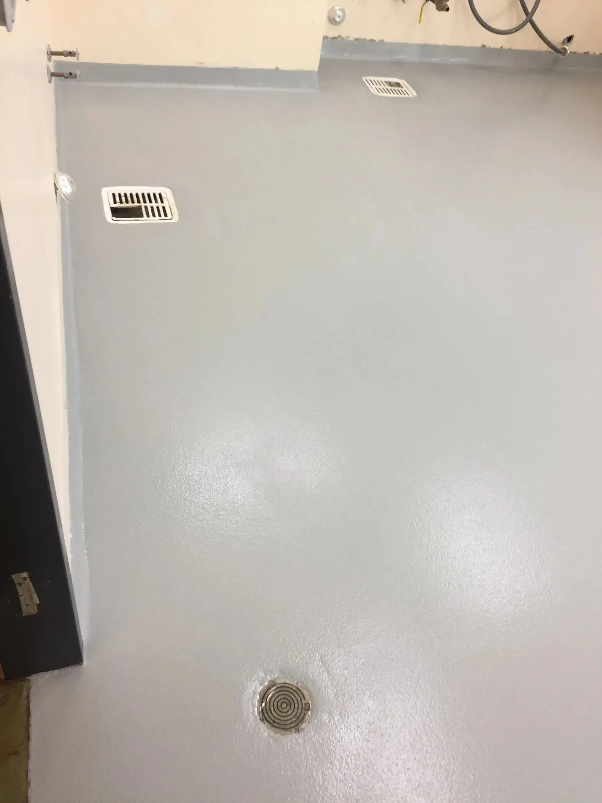 A gray, smooth floor with a drain and a sticker labeled