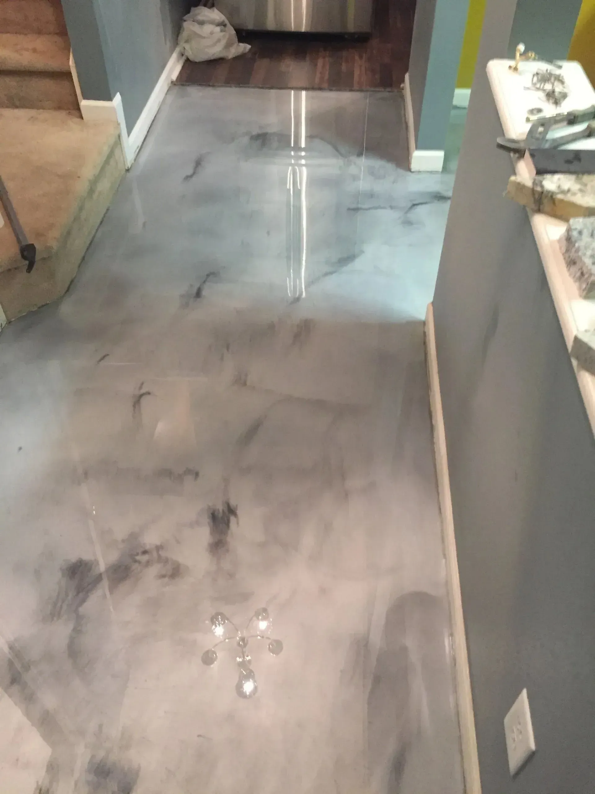 Metallic epoxy flooring in a hallway with gray walls and a wooden staircase.