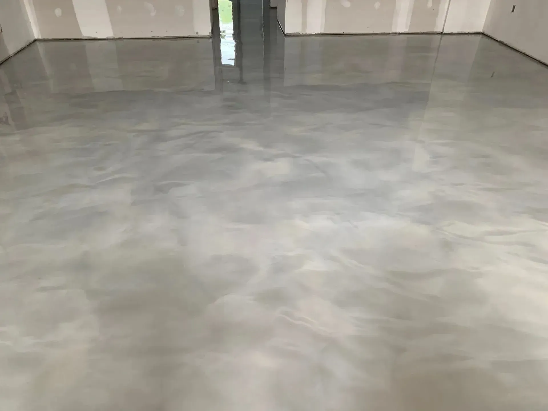 Metallic gray epoxy floor reflecting light in a room with unfinished walls.