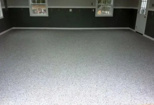 Empty garage with speckled grey floor, dark green walls, windows, and a white door.