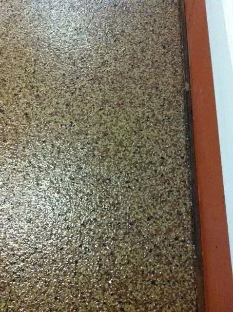 Close-up of a speckled, glossy floor with a brown edge and a white wall visible.