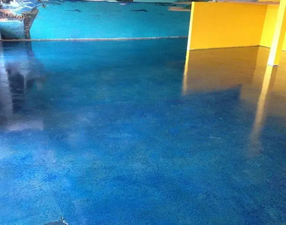 Blue stained concrete floor with glossy finish, reflecting a yellow wall and other elements.