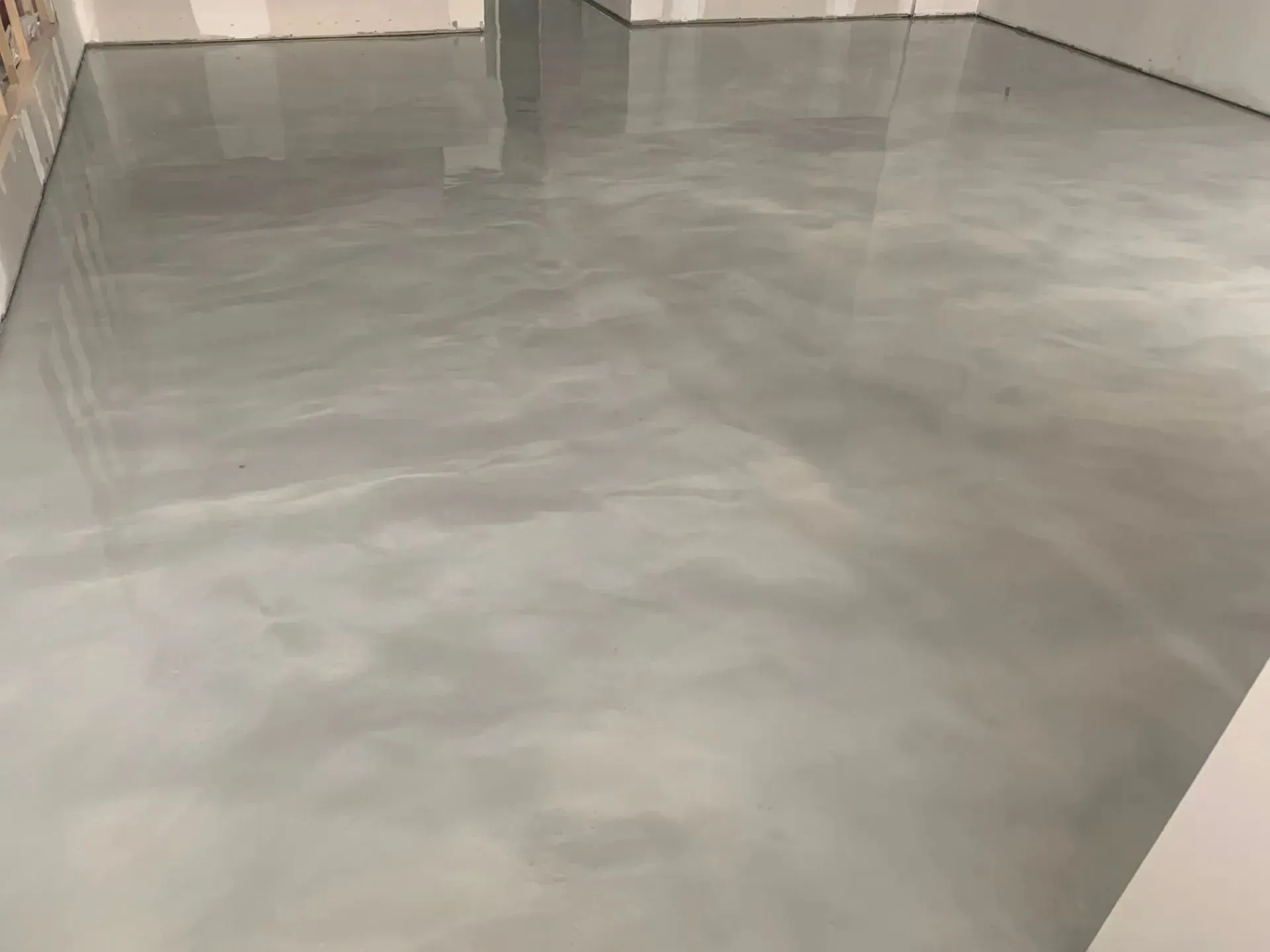 Shiny, light gray metallic epoxy floor in a room, reflecting light with subtle patterns.