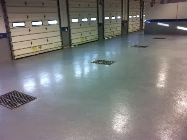 Garage interior with multiple closed overhead doors and a shiny, grey floor with grates.