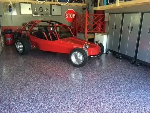 Red dune buggy in a garage with a speckled purple floor.