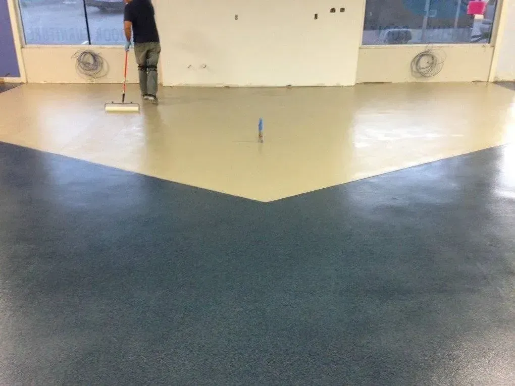 Person paints a floor with a roller. The floor is divided into beige and blue sections.