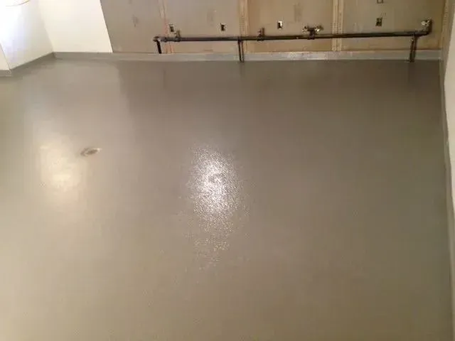 Gray epoxy floor with plumbing pipes on the wall above.