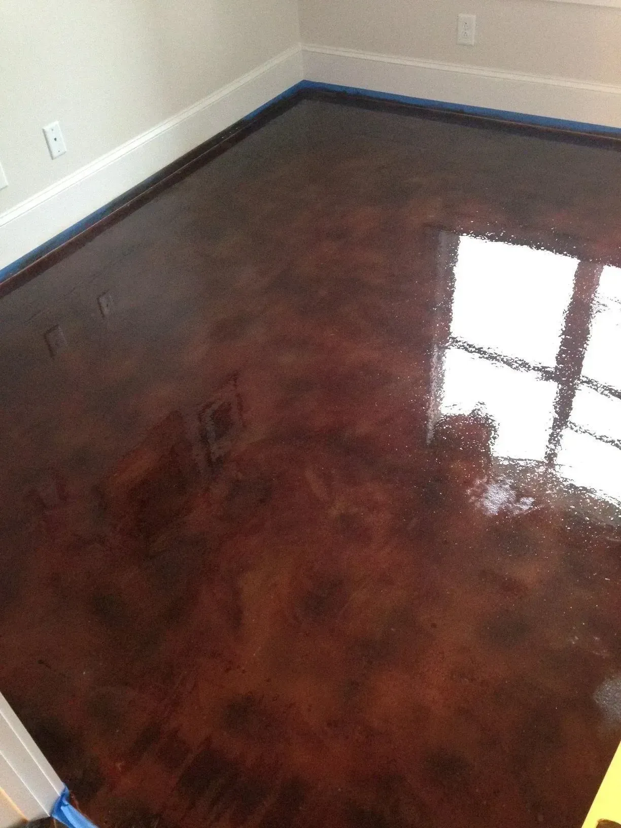 Metallic reddish-brown epoxy floor reflecting light from a window, next to white baseboards and walls.