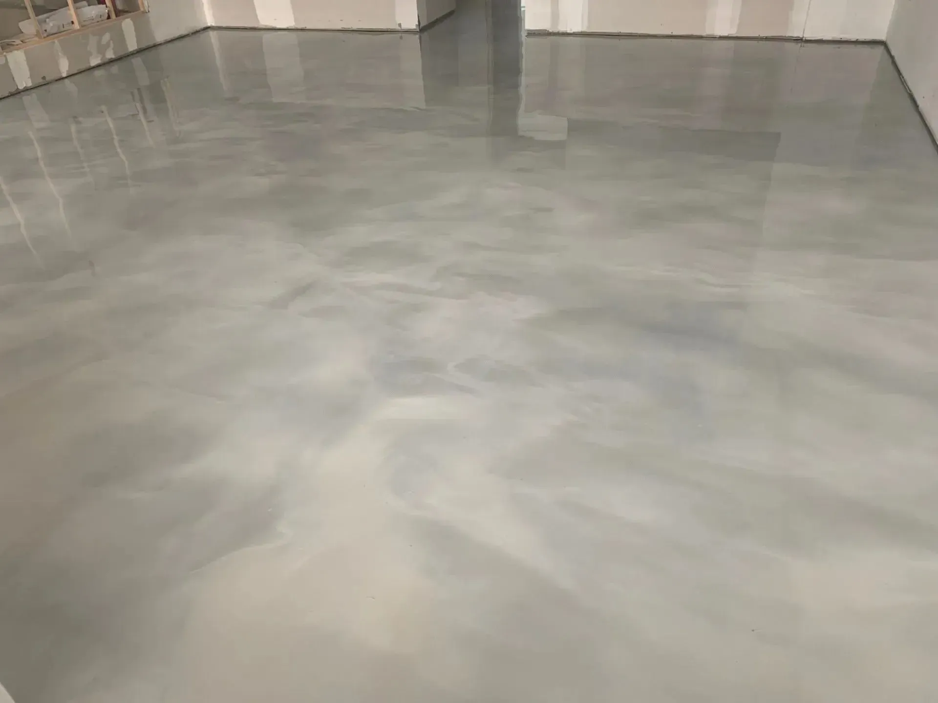 Shiny, light gray epoxy floor with swirling patterns, inside a room with unfinished walls.