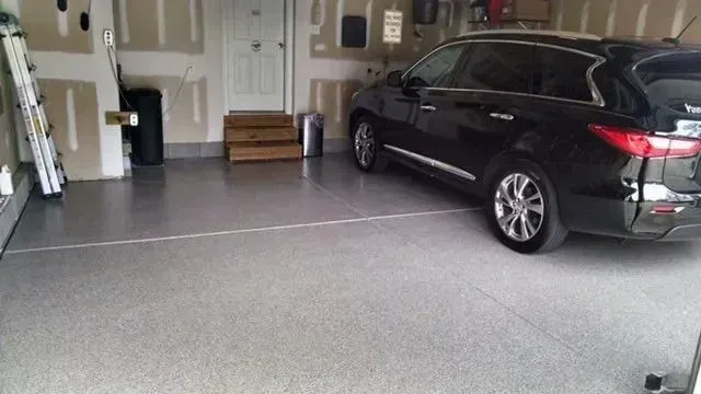Garage interior with black SUV parked on speckled gray floor. White door and shelves in the background.