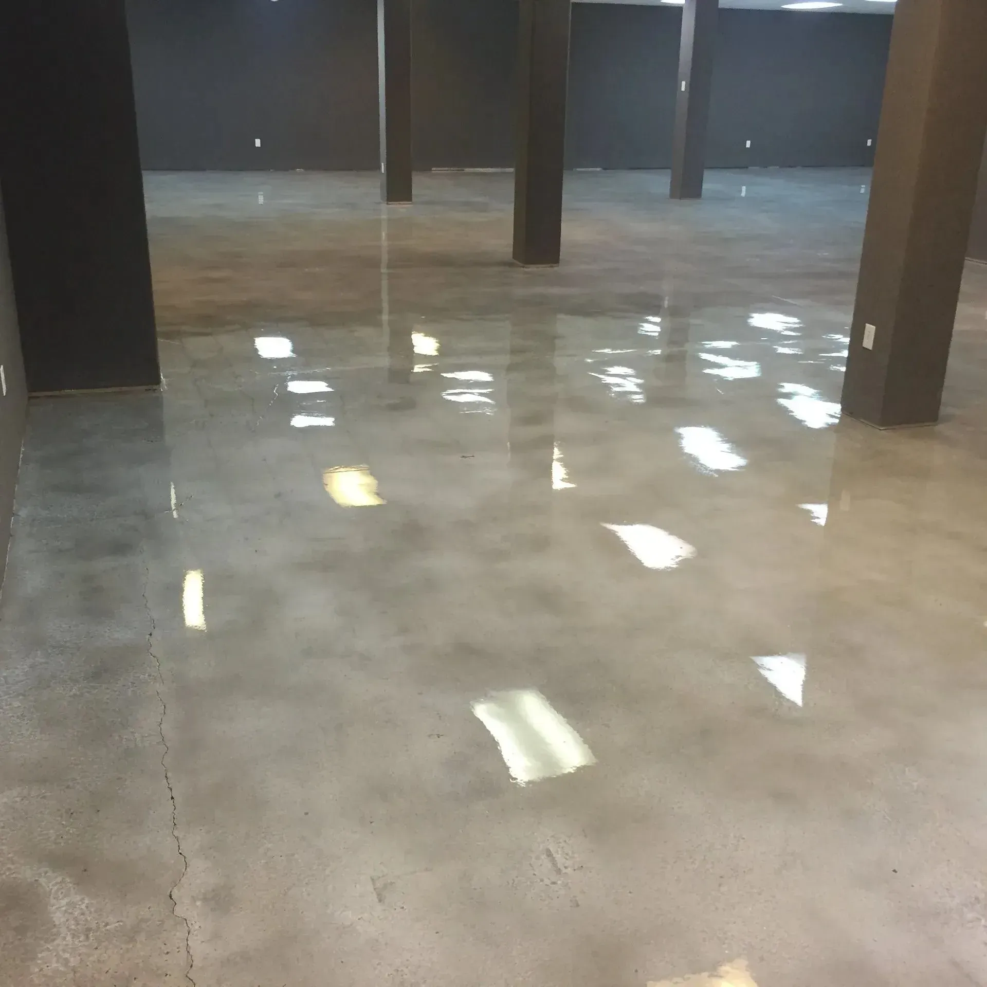 Polished concrete floor in an empty room, reflecting overhead lights. Dark gray columns and walls.
