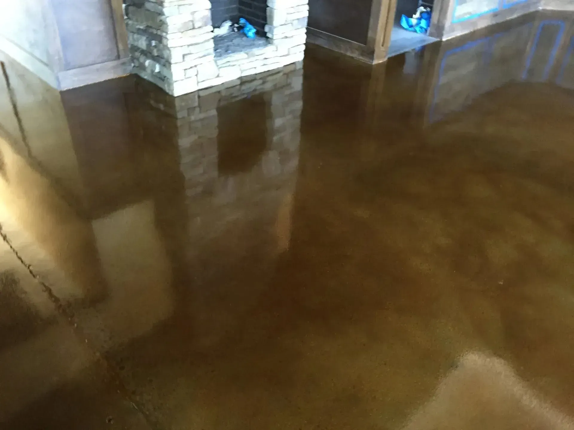 Brown stained and sealed concrete floor reflecting light with a stone fireplace in the background.