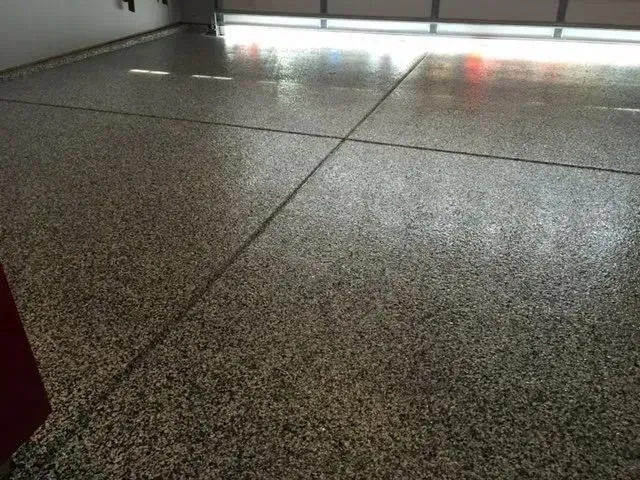 Gray speckled epoxy garage floor with dark seam lines, reflecting overhead light.