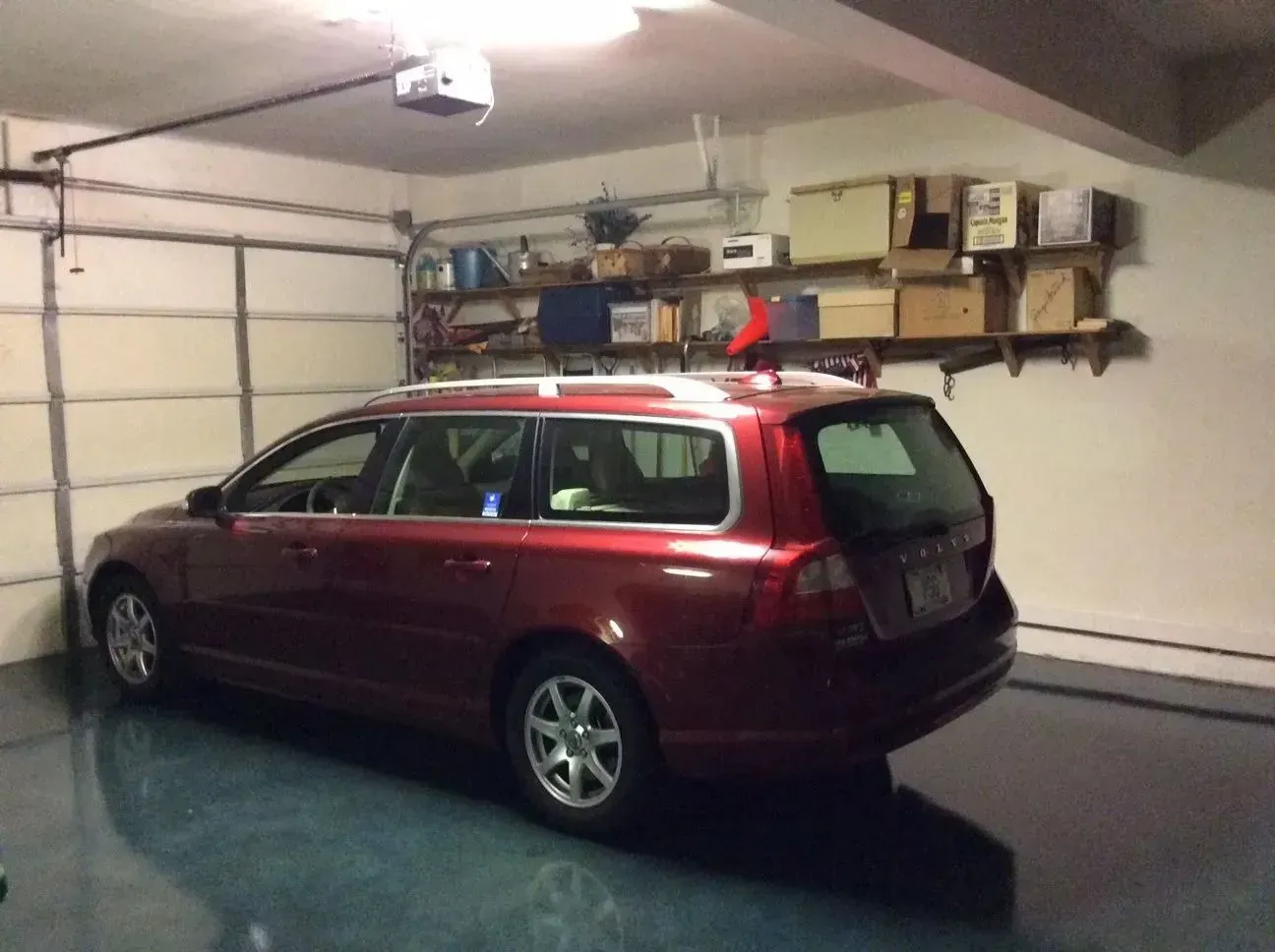 Red Volvo station wagon parked inside a garage. Shelves with boxes and items above the car. Garage door visible.