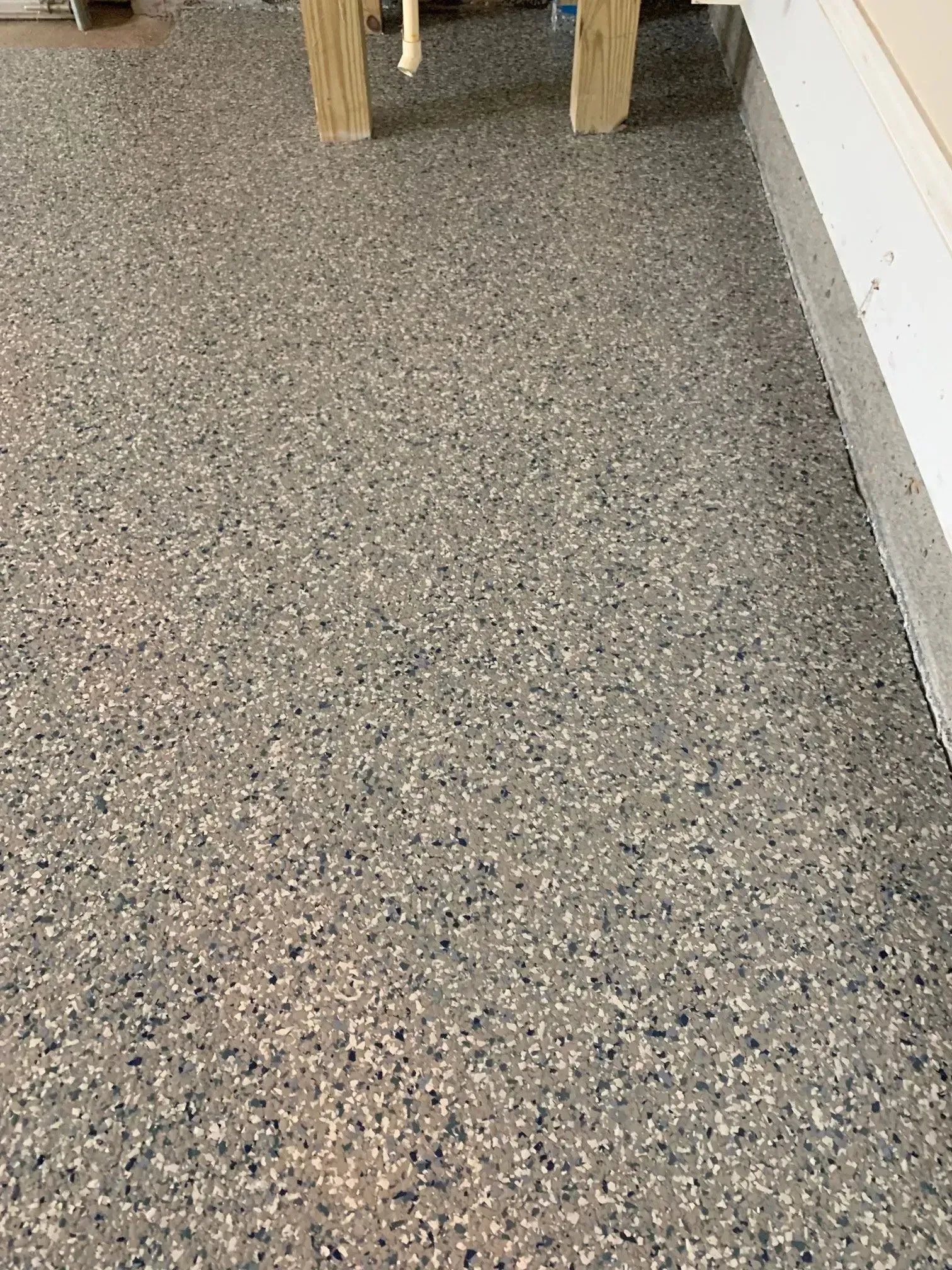 Gray speckled concrete floor with a portion of a wooden table leg and white wall.
