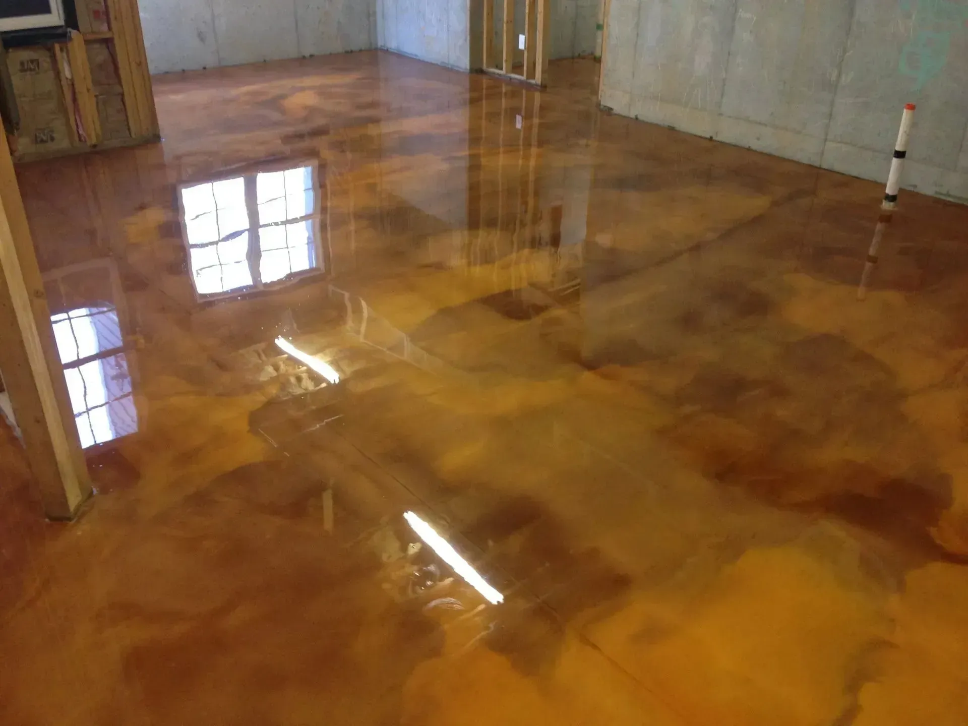 Metallic gold and brown epoxy floor in a room, reflecting light from a window and ceiling fixture.