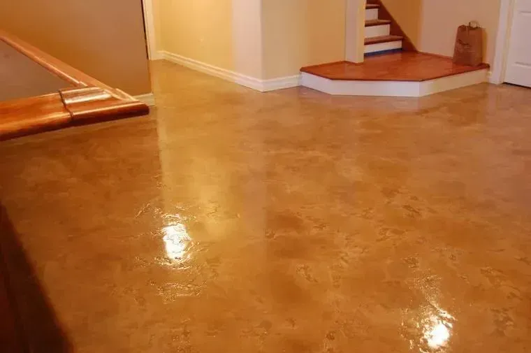 Polished, stained concrete floor in a room with a raised platform, wood trim, and a partially visible staircase.