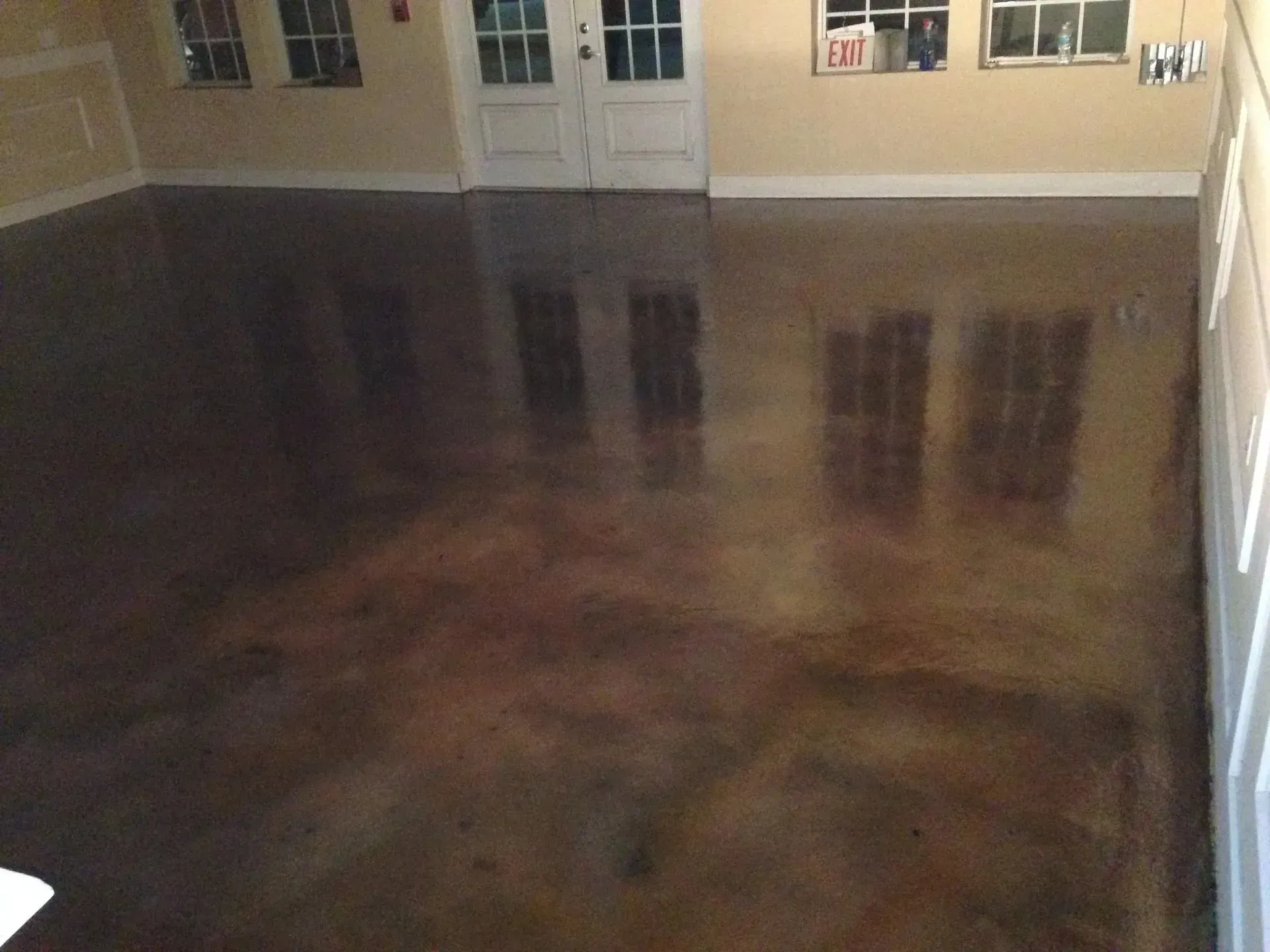 Dark, stained concrete floor with reflective sheen. Interior with multiple windows and white door.