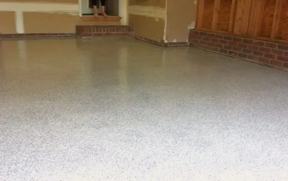 Garage floor with epoxy coating, light gray with speckles, brick base, and partially finished walls.