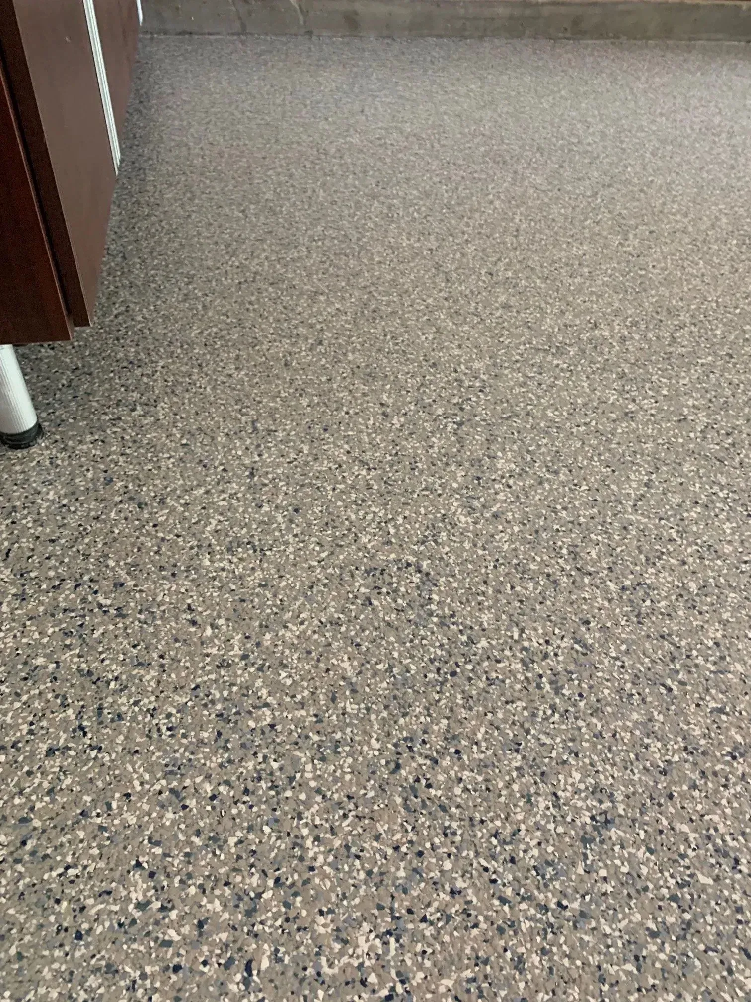 Speckled epoxy flooring in shades of gray, white, and blue. A brown cabinet's edge is visible.