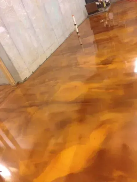 Shiny, amber-colored epoxy floor with marbled effect, reflecting light. A concrete wall is in the background.