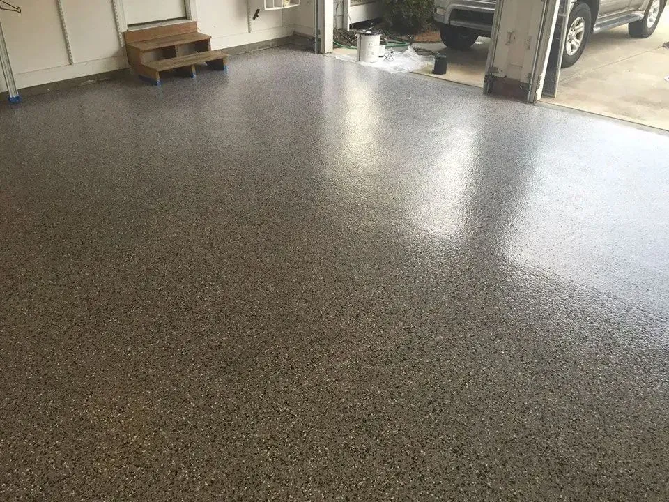 Epoxy-coated garage floor with speckled gray and brown finish, reflecting light.