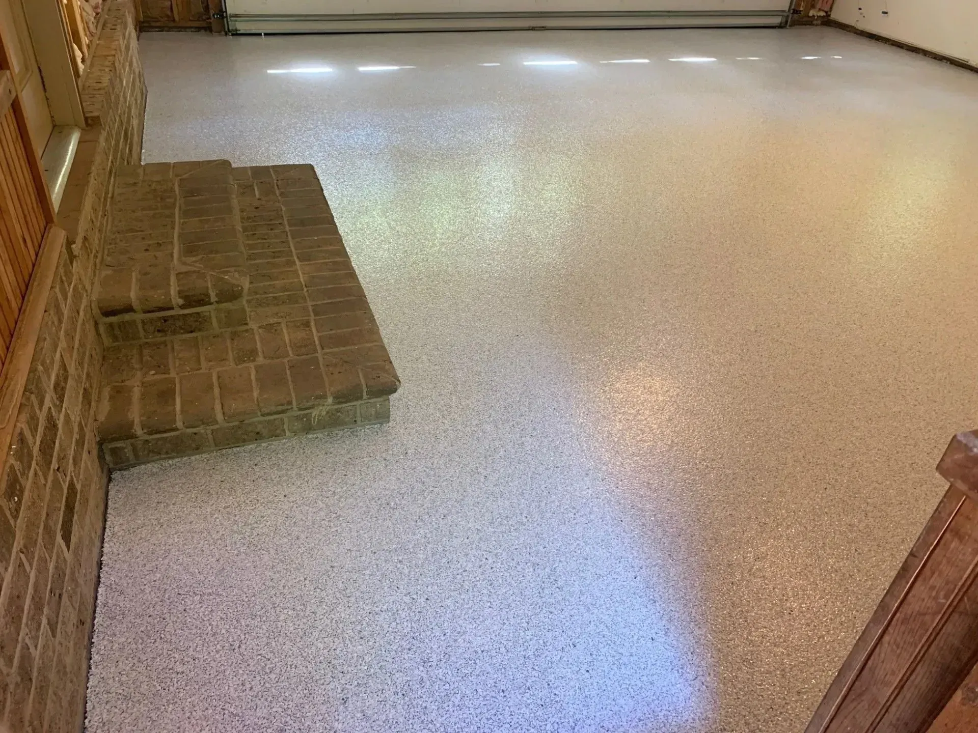 Garage with speckled, light-colored epoxy flooring and brick steps. Bright overhead light.